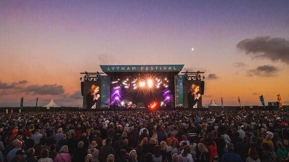 Large crowd watching a concert. Stage with screens and lights.