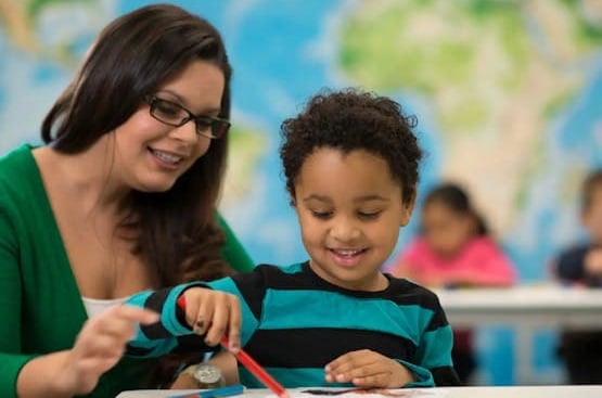 A woman helping a child color at school.