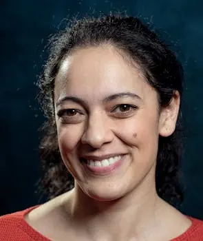 A woman with dark hair smiles at the camera. She wears a red top.