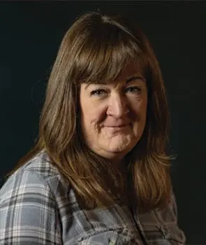 Woman with brown hair, in a plaid shirt, looking at the camera.