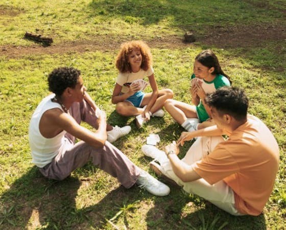 Four friends sitting on the grass, playing cards.
