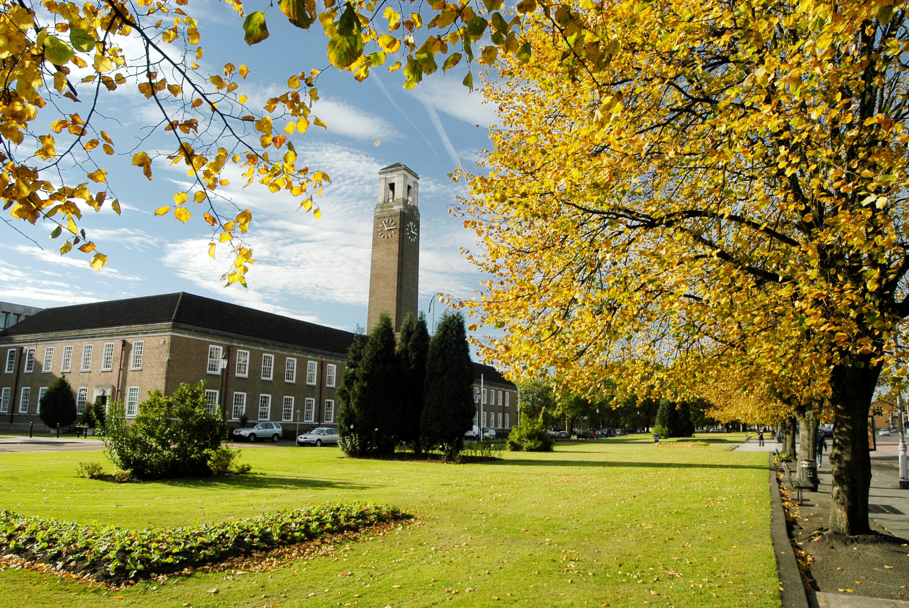 Building, tall clock tower, trees with yellow leaves. Blue sky with clouds.