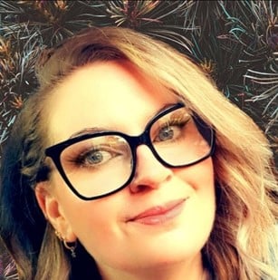 Woman with glasses smiling and wearing a sweater.