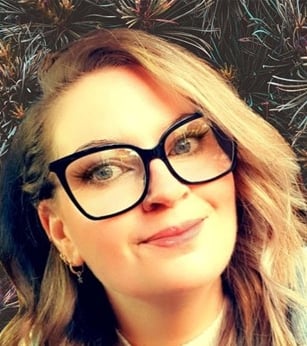 Woman with glasses smiling and wearing a sweater.