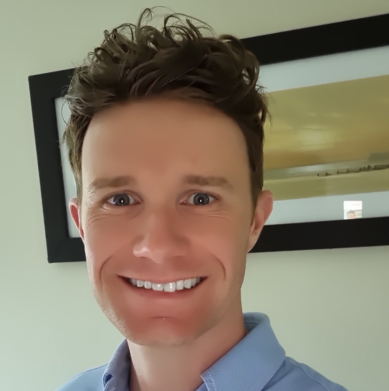Smiling man in a blue button-down shirt, looking at the camera.