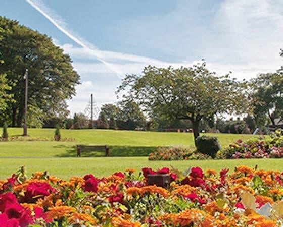 Park with flowers, trees, benches, and green grass.