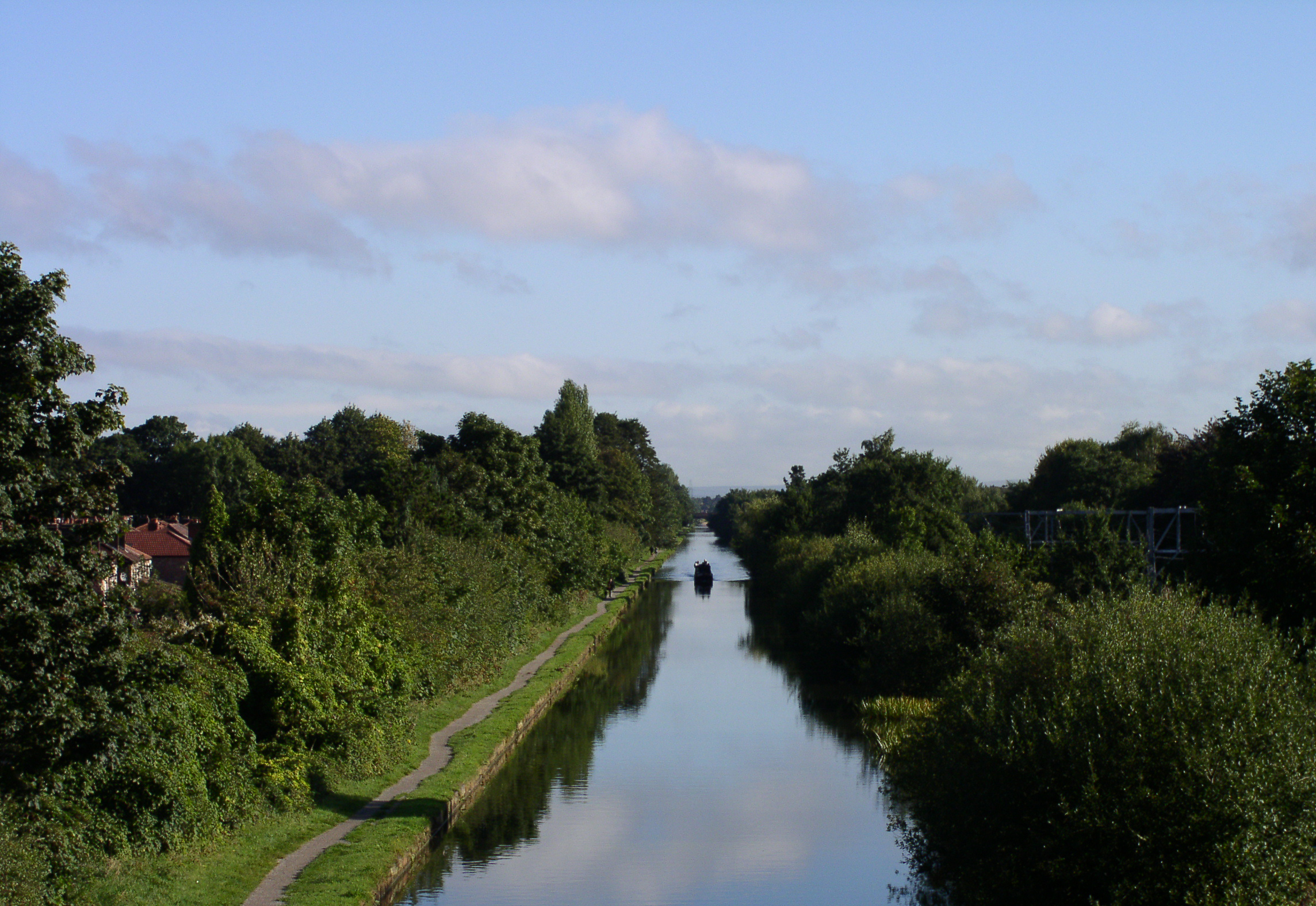 Canal with water reflecting the sky, flanked by greenery and paths, with a boat.