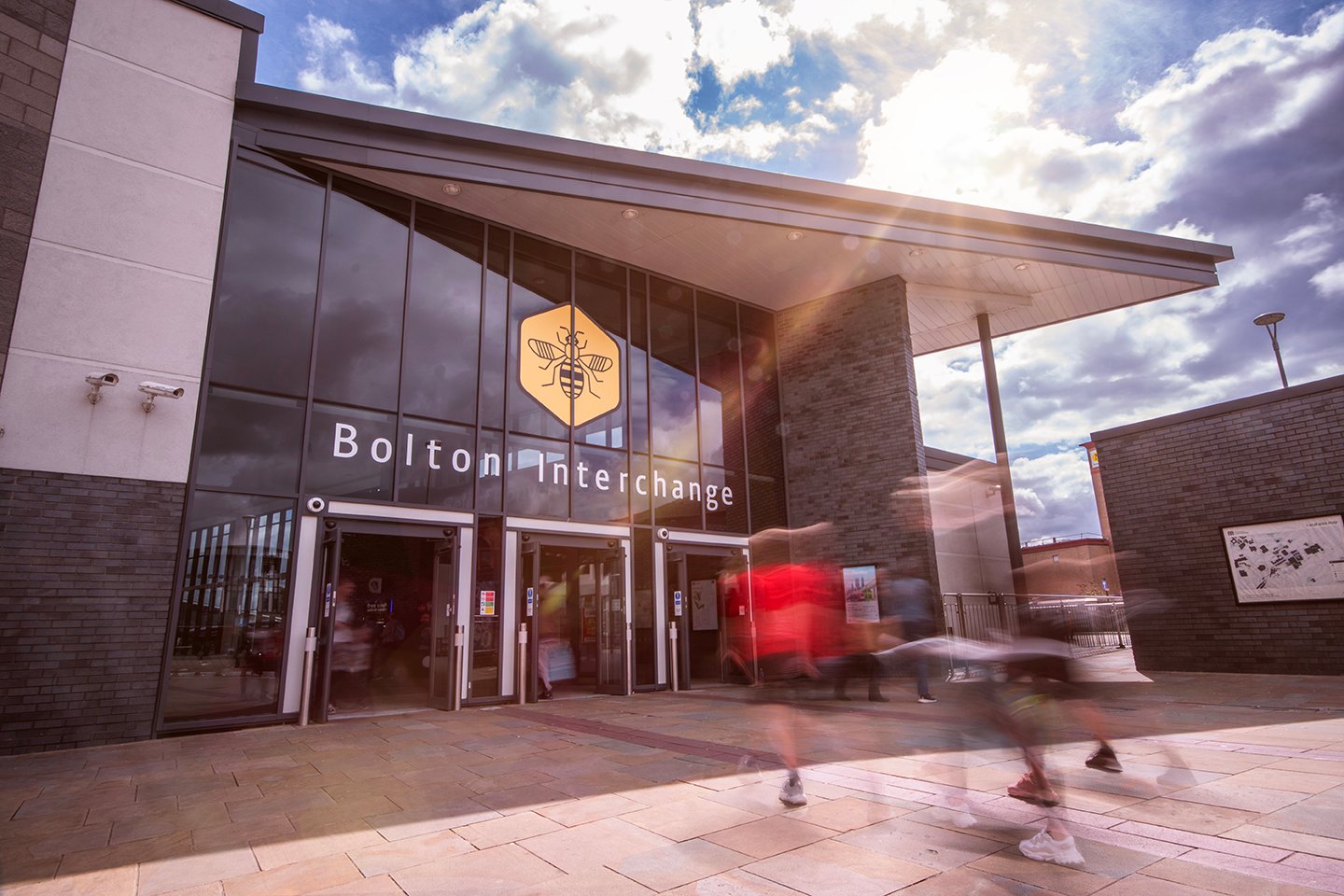 Modern building with people moving blurred. "Bolton Interchange" sign visible.