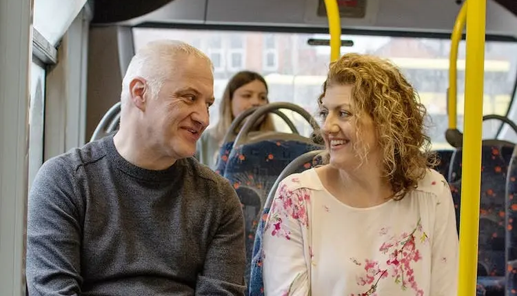 Couple smiling on a bus with a third passenger in the background.