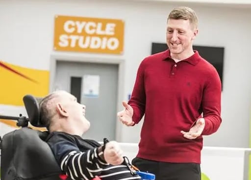 Man in wheelchair smiling at a person, "Cycle Studio" sign in the background.