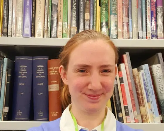Woman smiles in a library with books on shelves behind her.