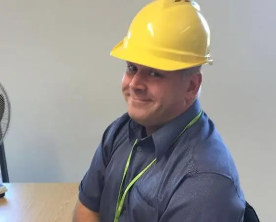 Man wearing yellow hard hat, blue shirt, and a green lanyard.