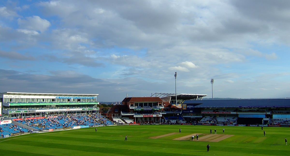 Cricket stadium with green field and blue sky.