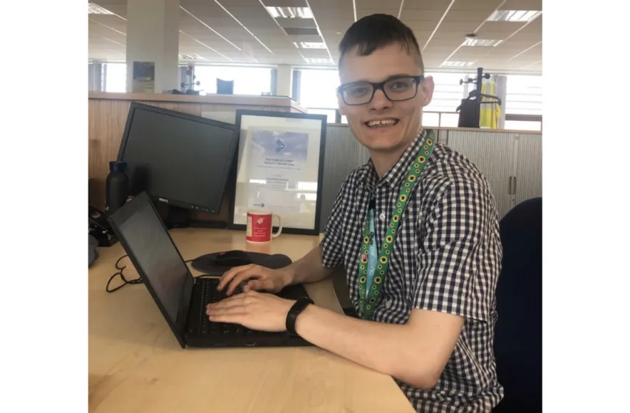 A man working on a laptop at a desk, smiling.
