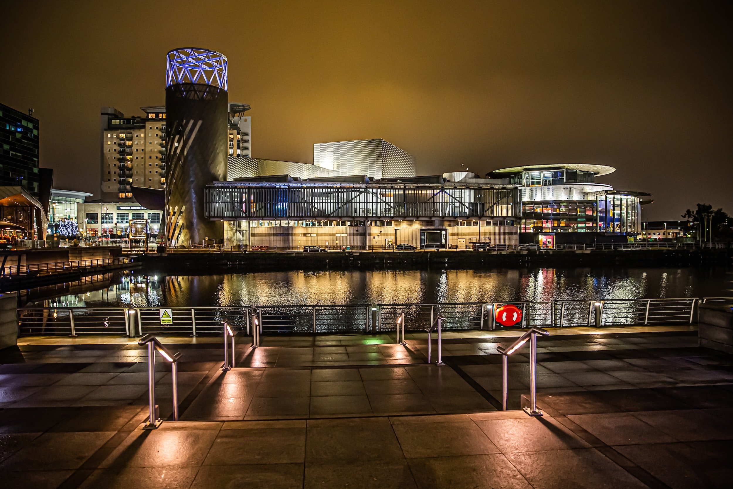 Buildings by the water at night, with lights reflected in the water.