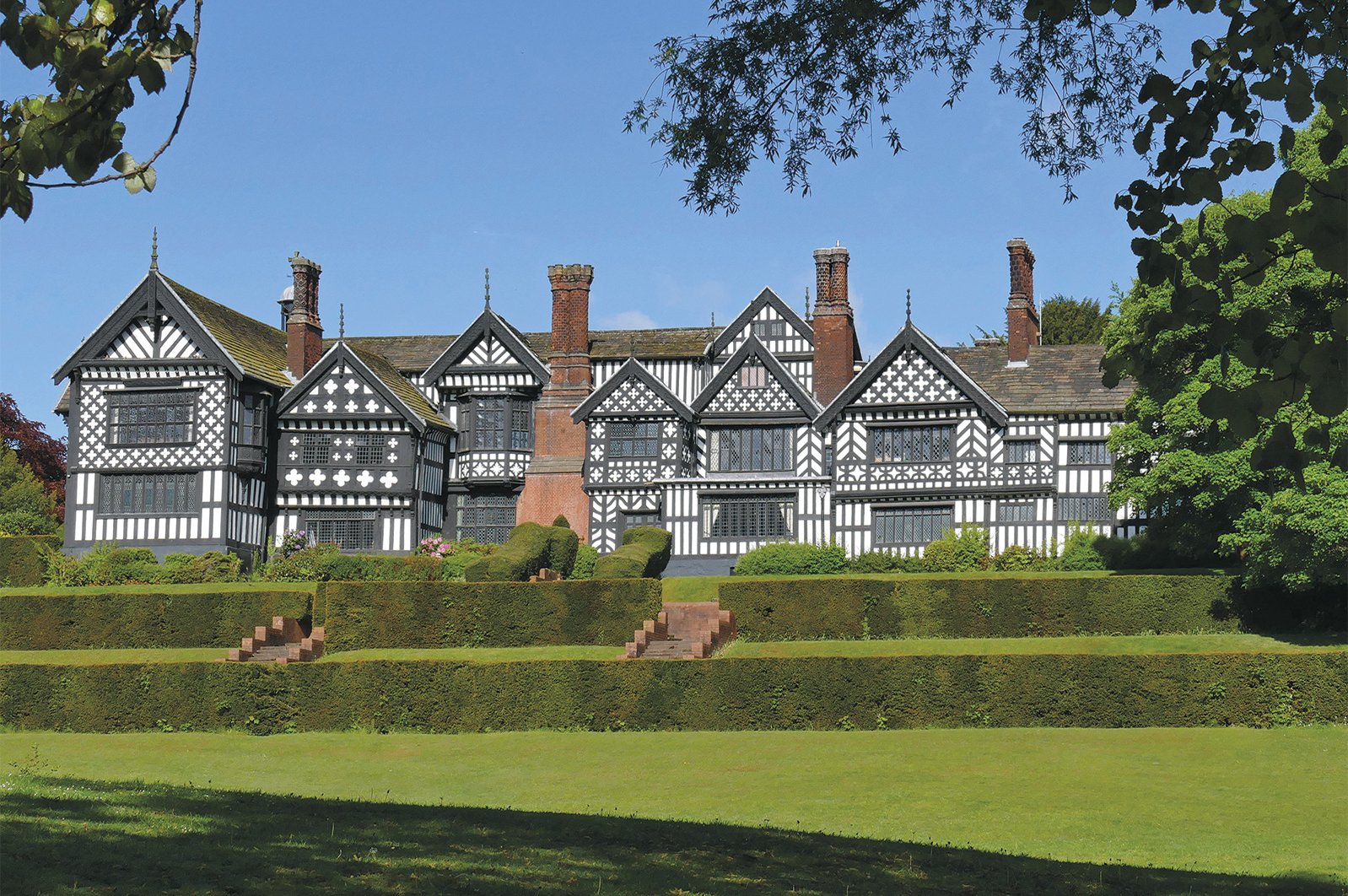 Black and white Tudor-style mansion with chimneys and landscaping.