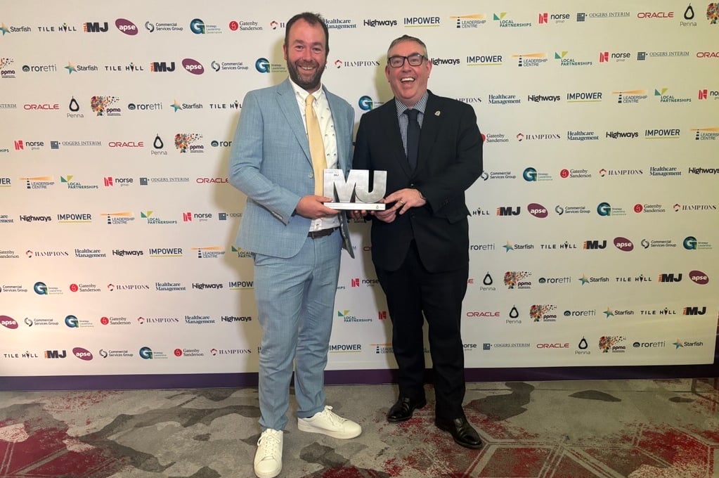 Two men holding award in front of a backdrop with logos.
