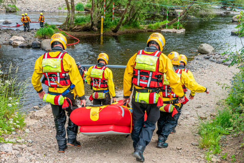 Team carrying a rescue stretcher near a river.
