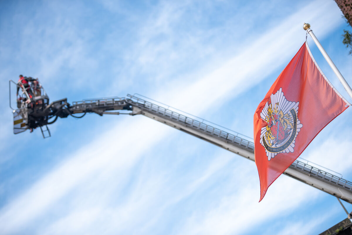 Fire truck ladder with people, a red flag and blue sky.