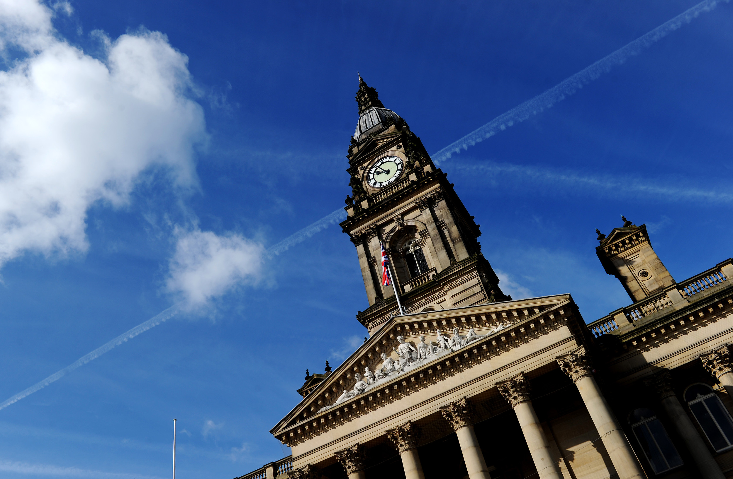 Low angle of a building with a clock tower and a flag against a blue sky.