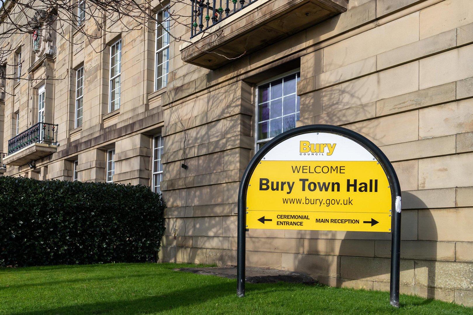 Bury Town Hall sign, building, greenery, bright day.