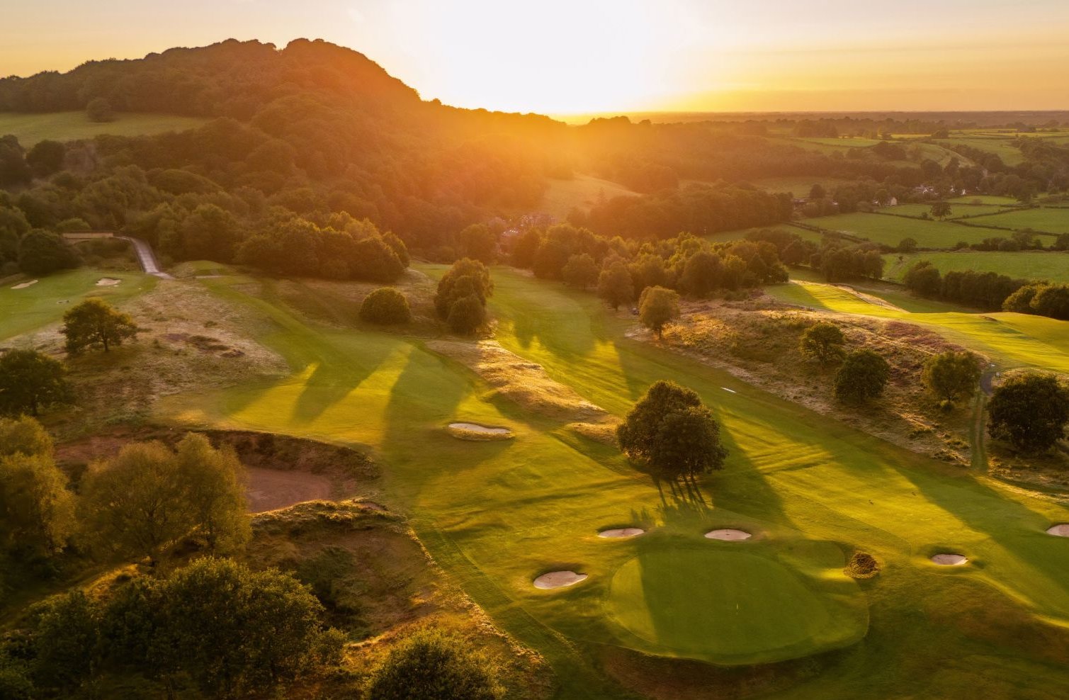 Aerial view of golf course with sunset, trees, and sand traps.