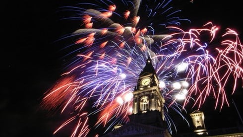 Fireworks burst over a building with clock tower.