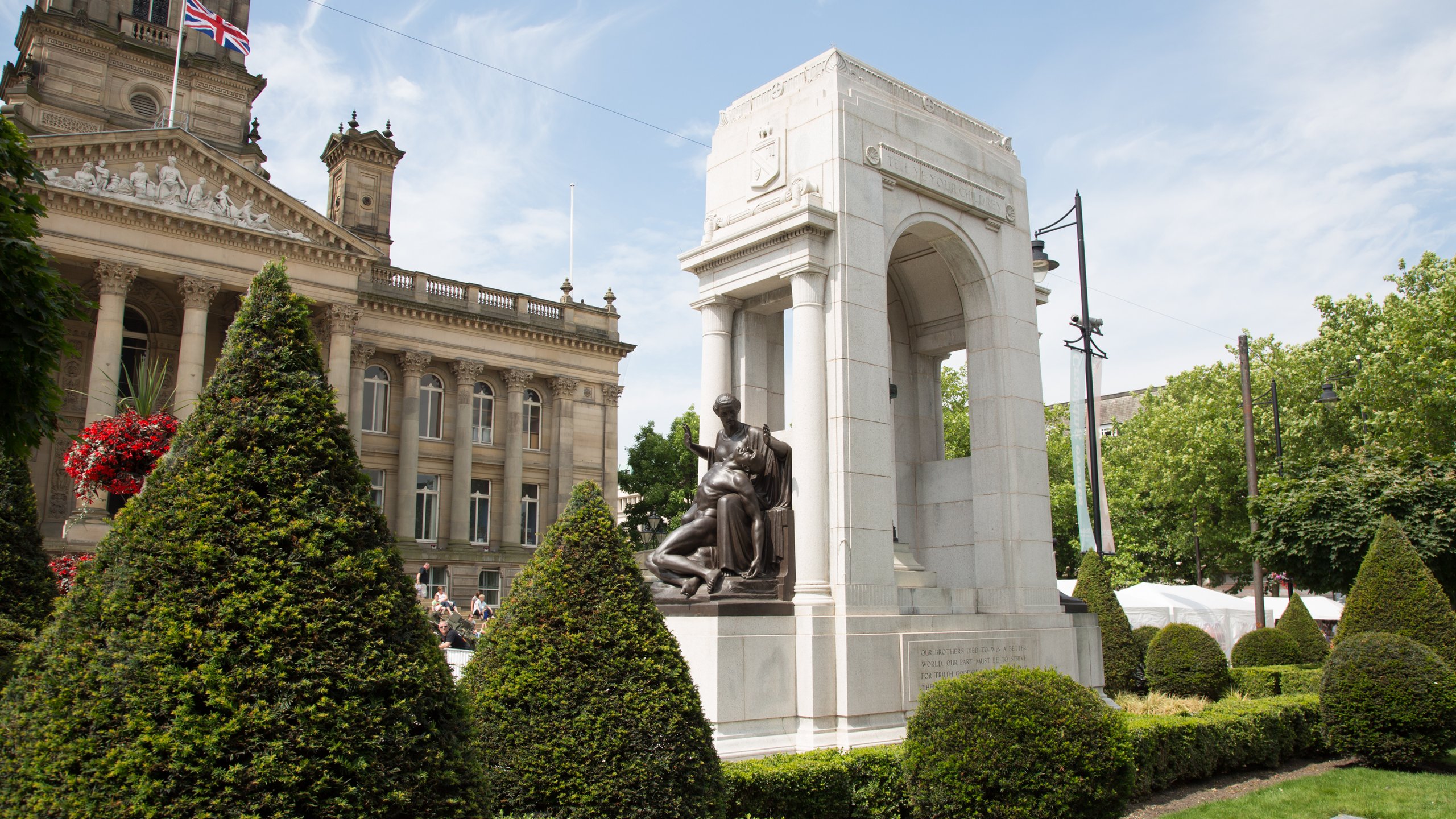 Memorial with sculpture, formal garden and historical building.
