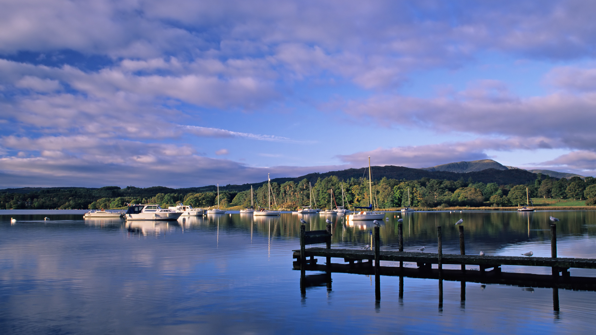 Boats docked on Lake Windermere with a view of the mountains and the sky.