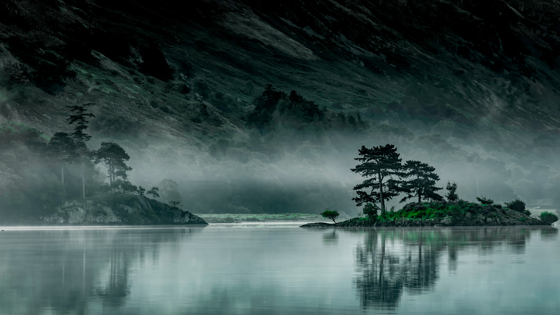 Lakescape with island of trees and misty mountains in the background.