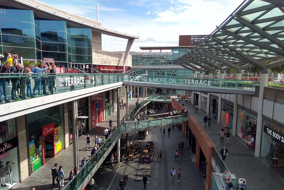 People walking on the terraces of a shopping mall, with shops visible.