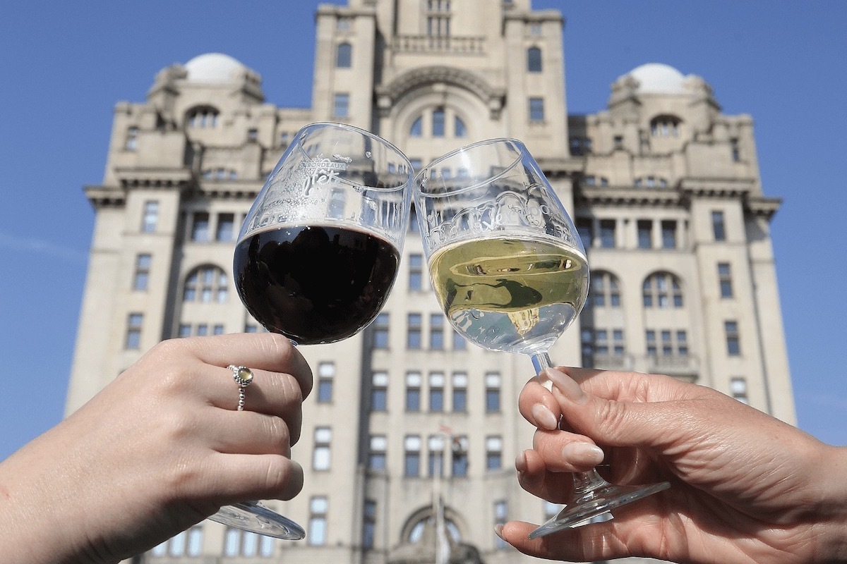 Two wine glasses clink in front of a building. One has red wine, the other white.