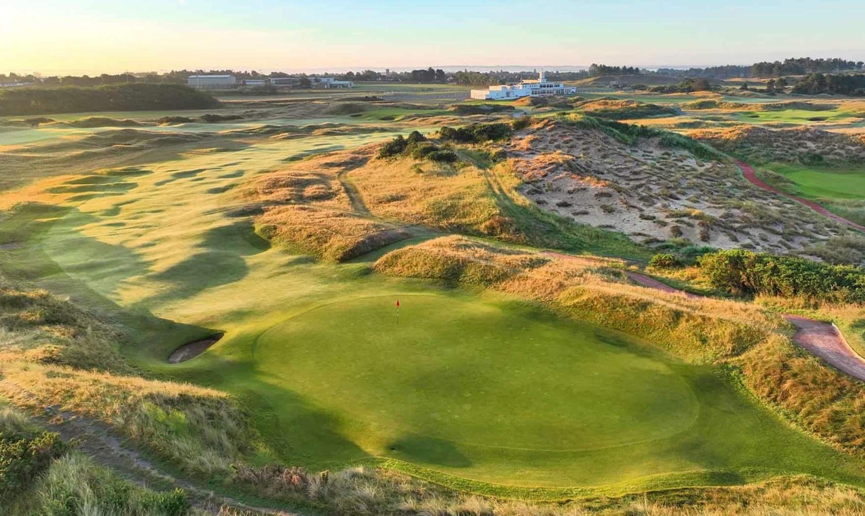 Aerial view of the Royal Birkdale golf course. Green with red flag. Sand dunes in the background.