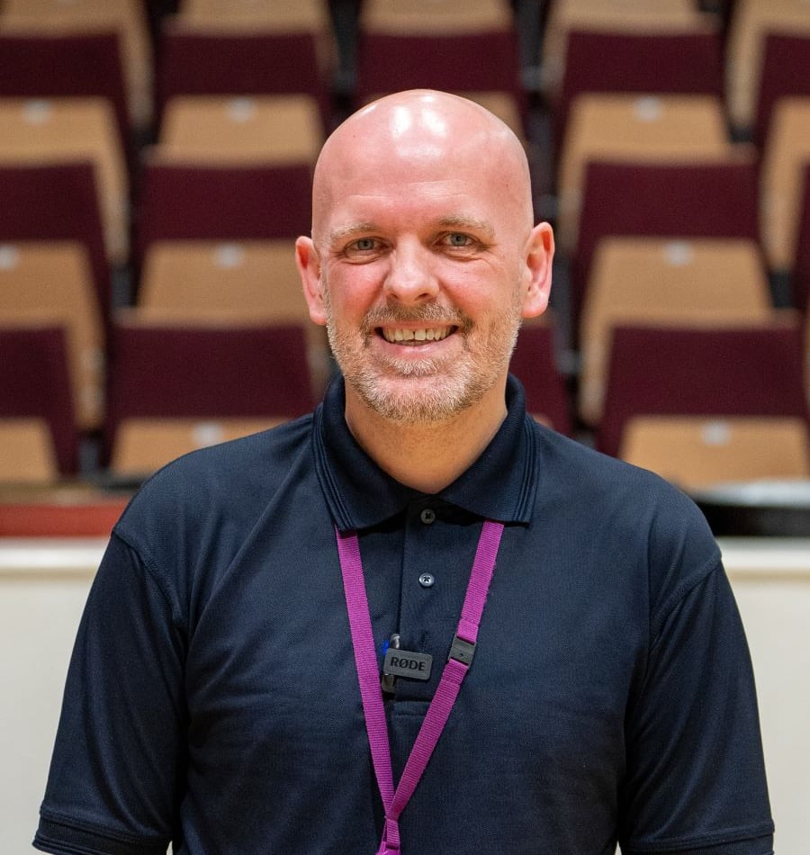 Bald man with a beard smiling, wearing a blue shirt and a lanyard.