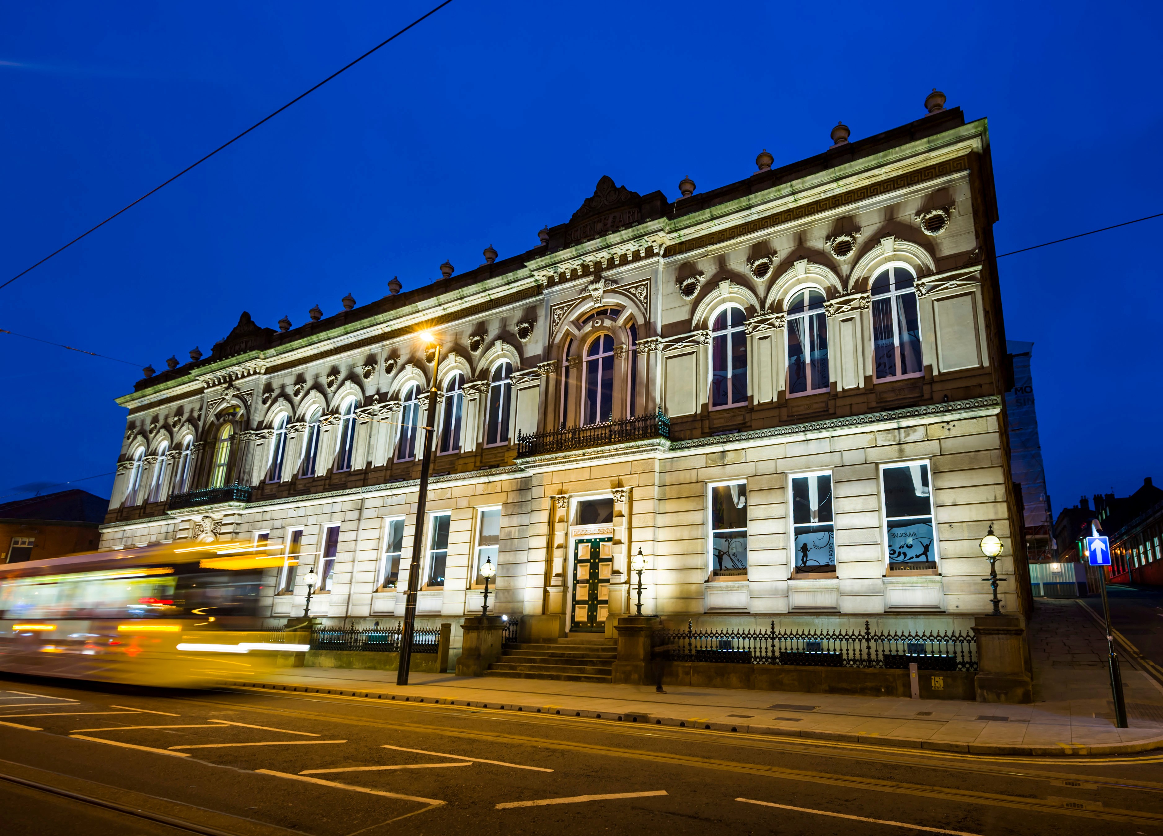 A building illuminated at night with a blurred bus passing by.