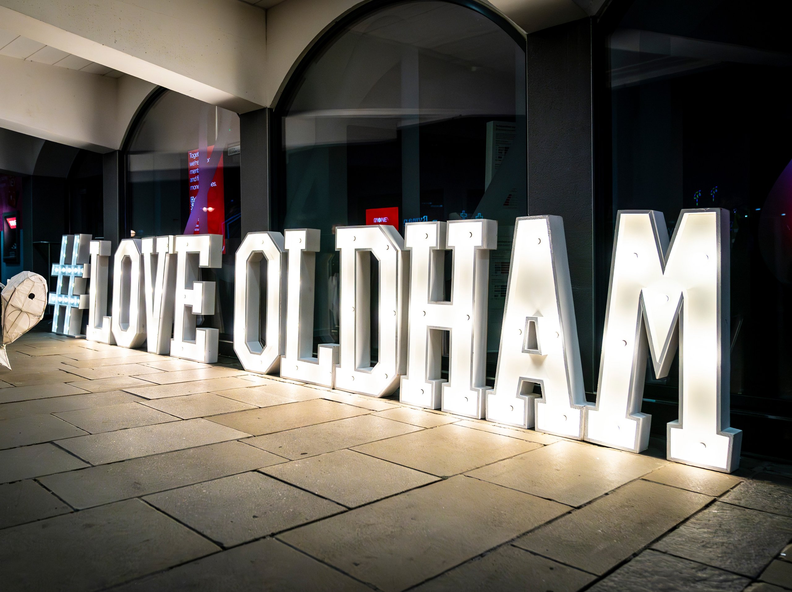 Lit-up sign reading #LOVE OLDHAM. Person carrying a lantern.