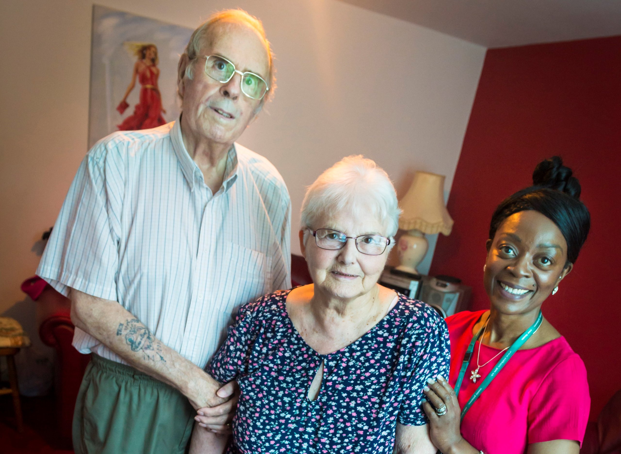 Elderly couple with caregiver in a home, with a walking aid.