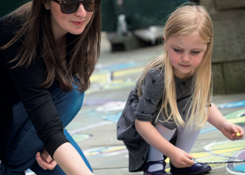 Woman and child drawing with chalk on sidewalk.