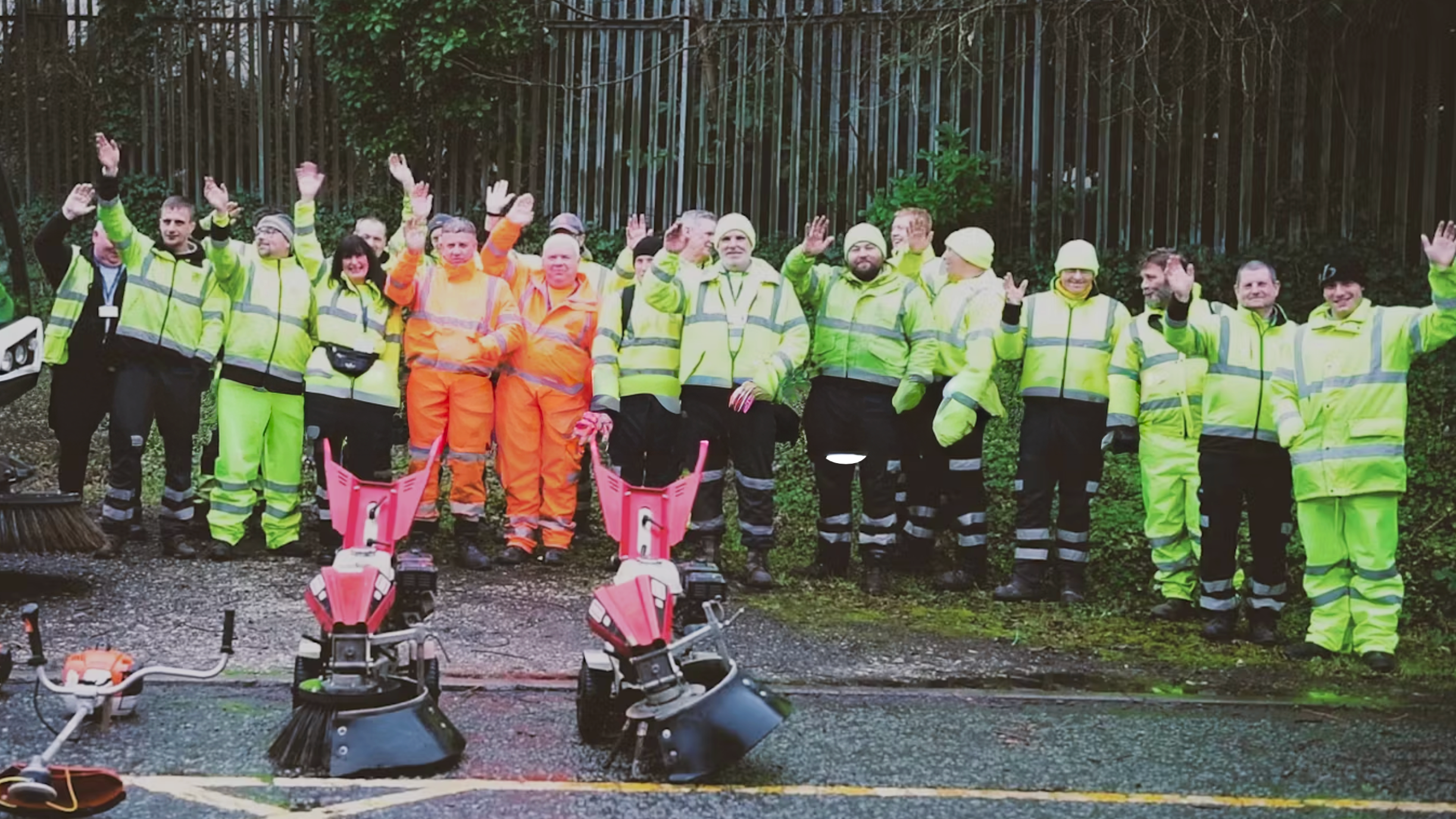 Group of environmental workers waving in uniform, with street cleaning equipment.