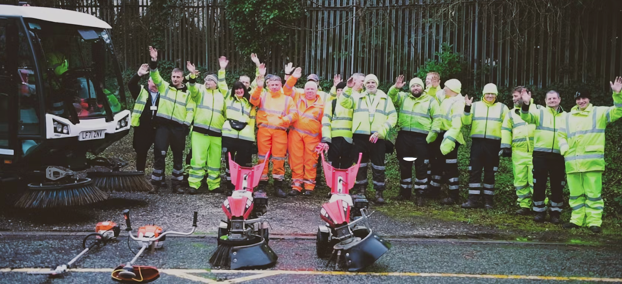 Group of environmental workers waving in uniform, with street cleaning equipment.