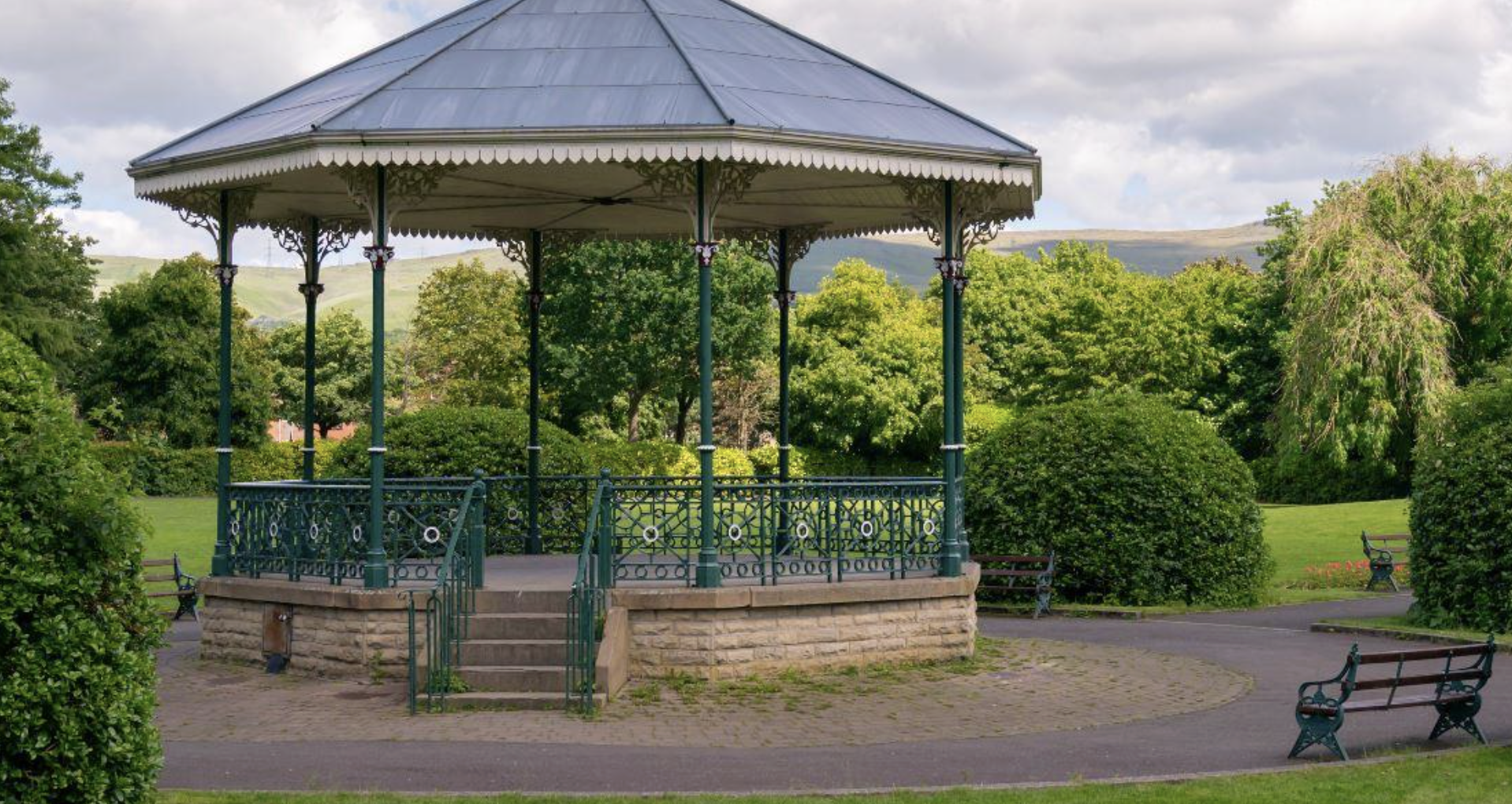 Bandstand surrounded by trees, benches, and a paved walkway.