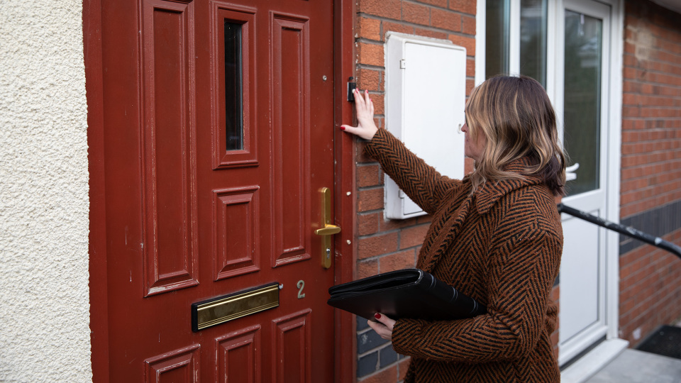 Woman ringing the doorbell of a house, holding a black folder.