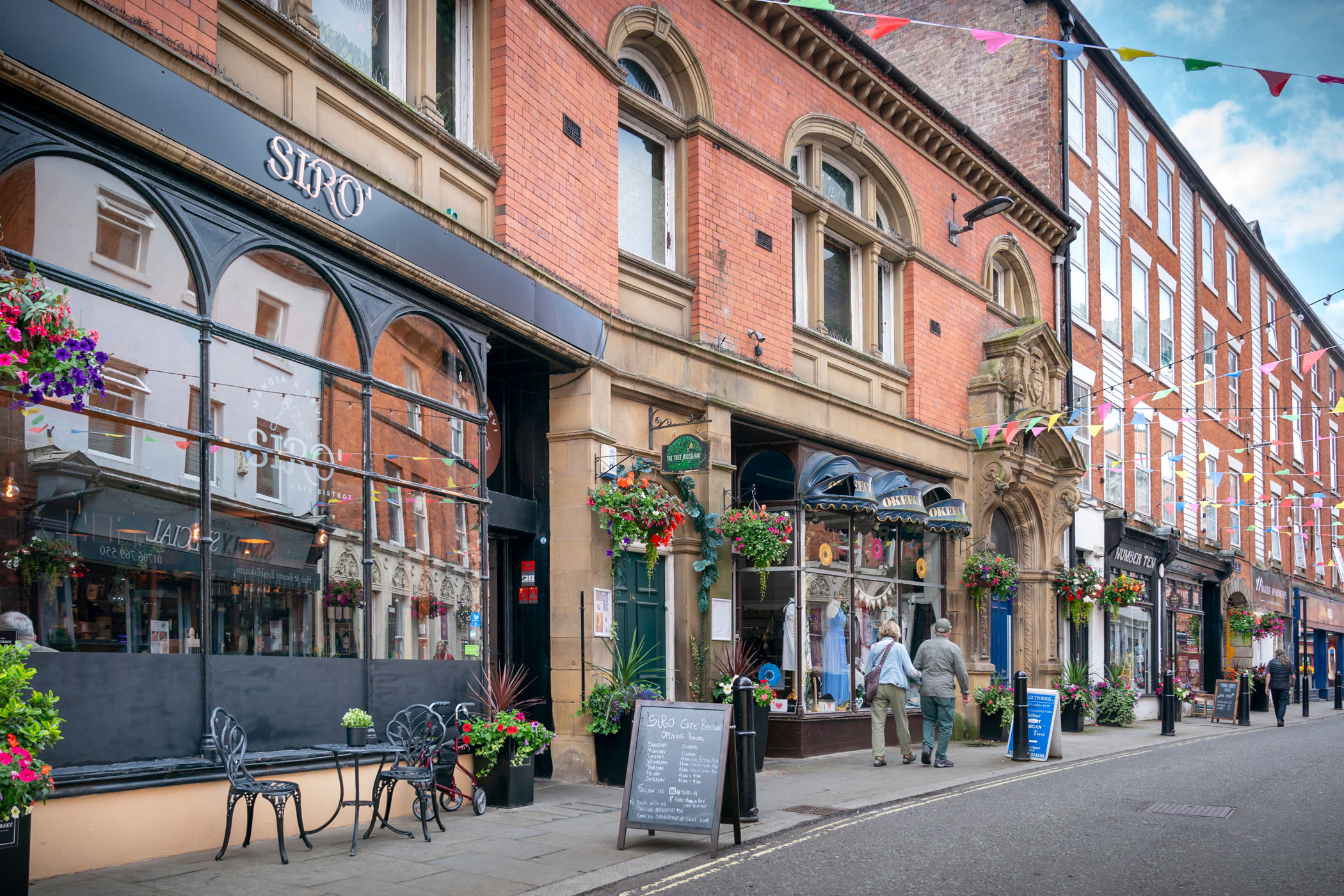 Shops and cafes on Baillie Street, with flower baskets and flags.