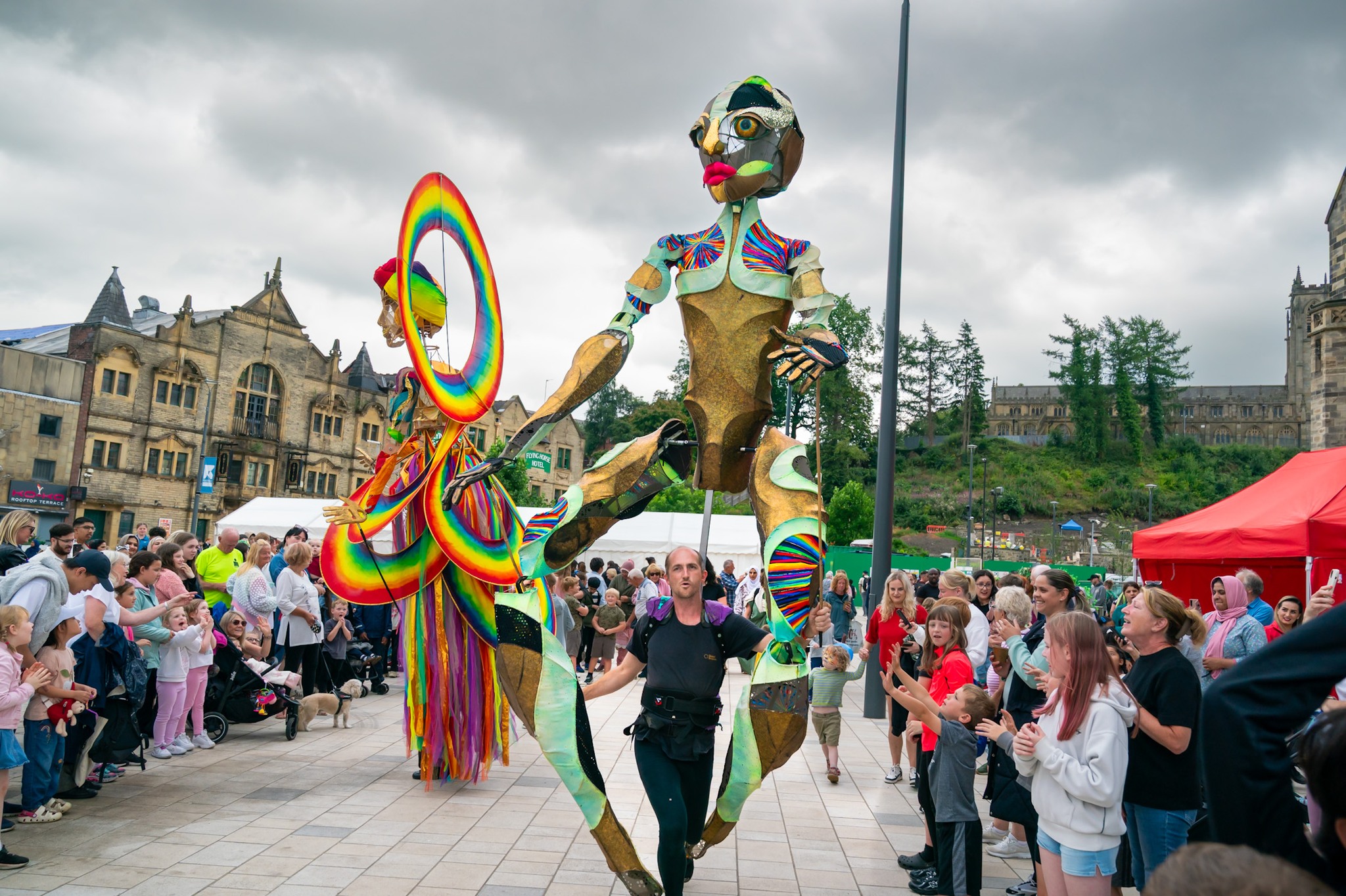 Giant puppets parade, crowds watching.