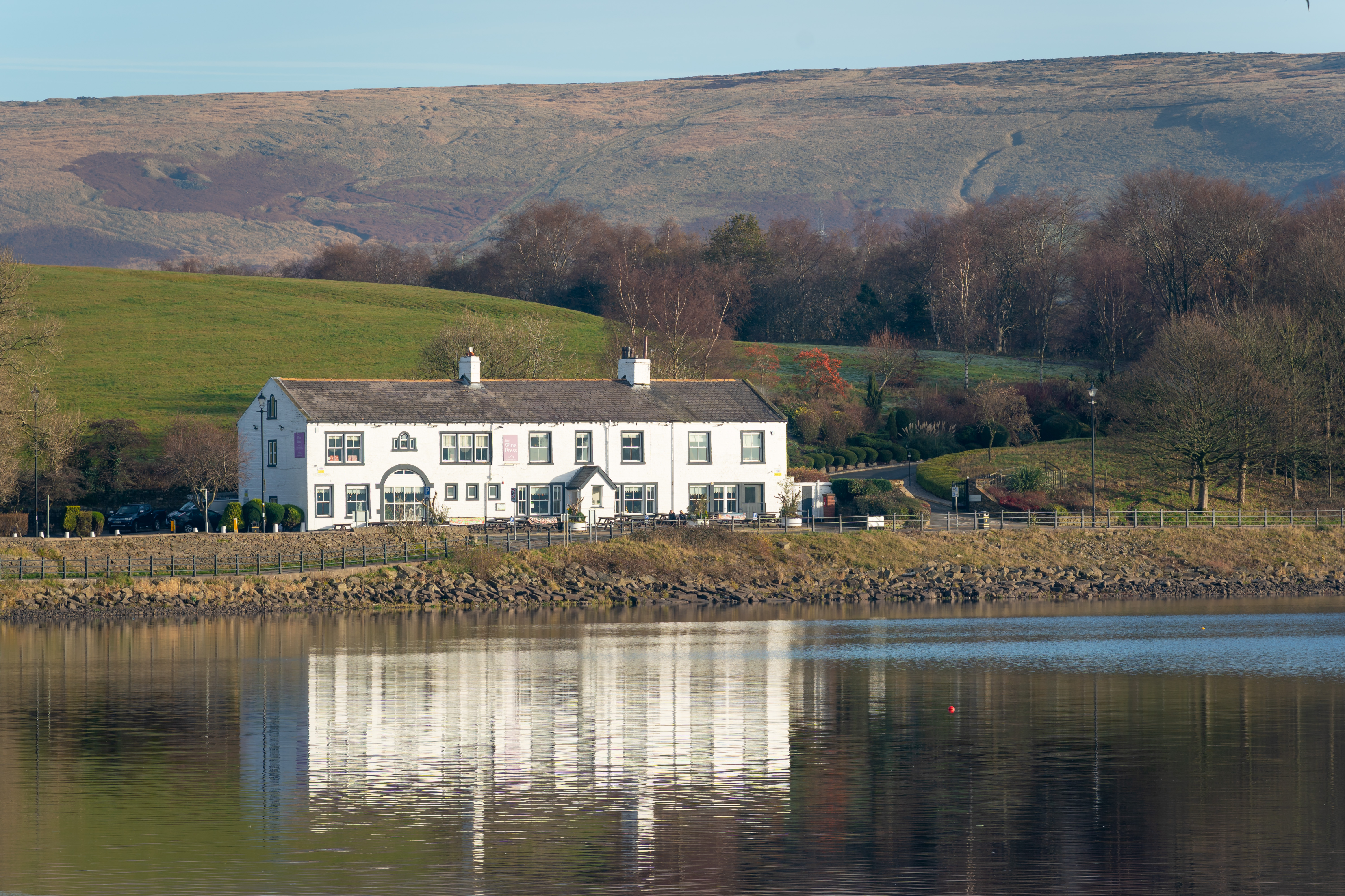 White building near a lake with hill in the background.