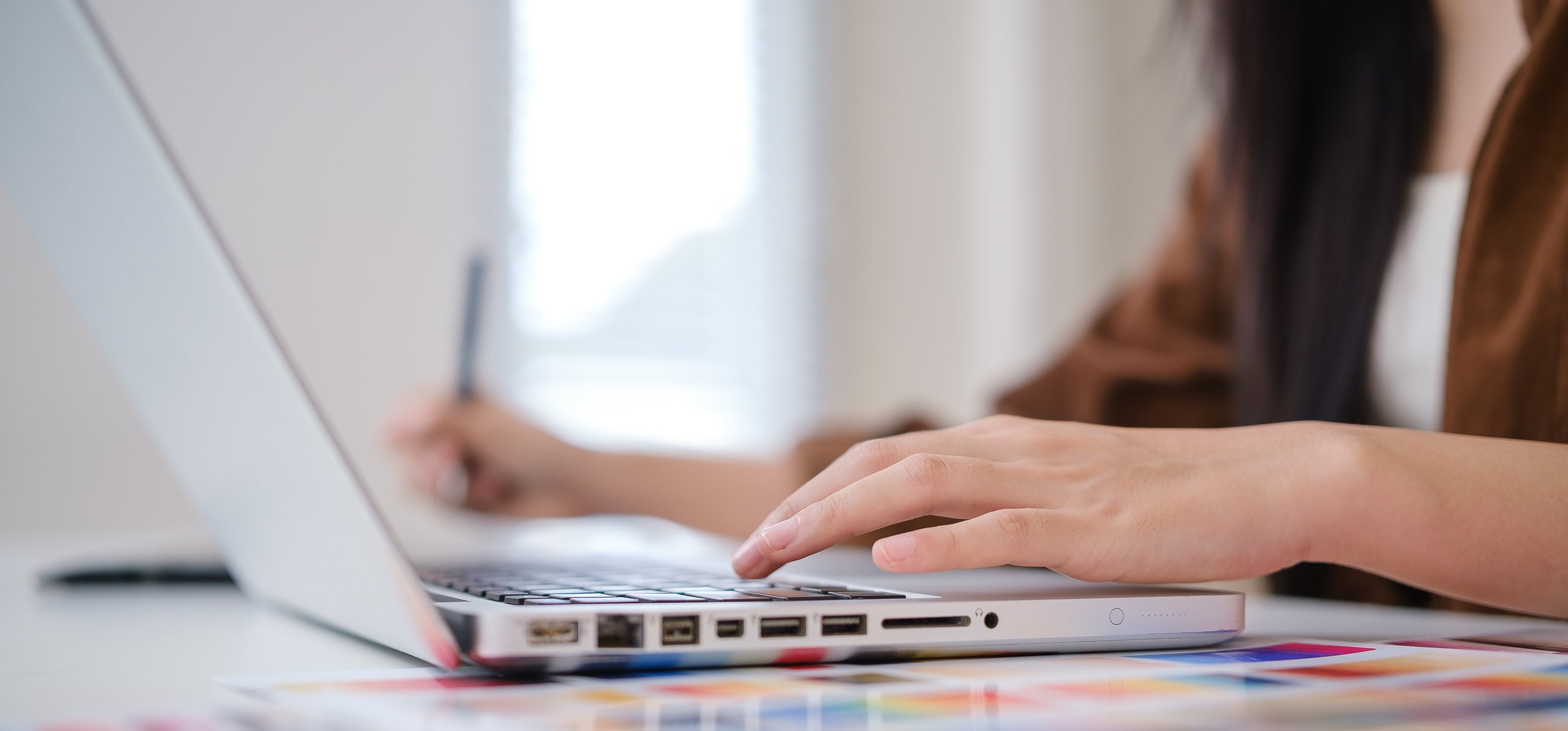 A person's hands are on a laptop, with color swatches in the foreground.