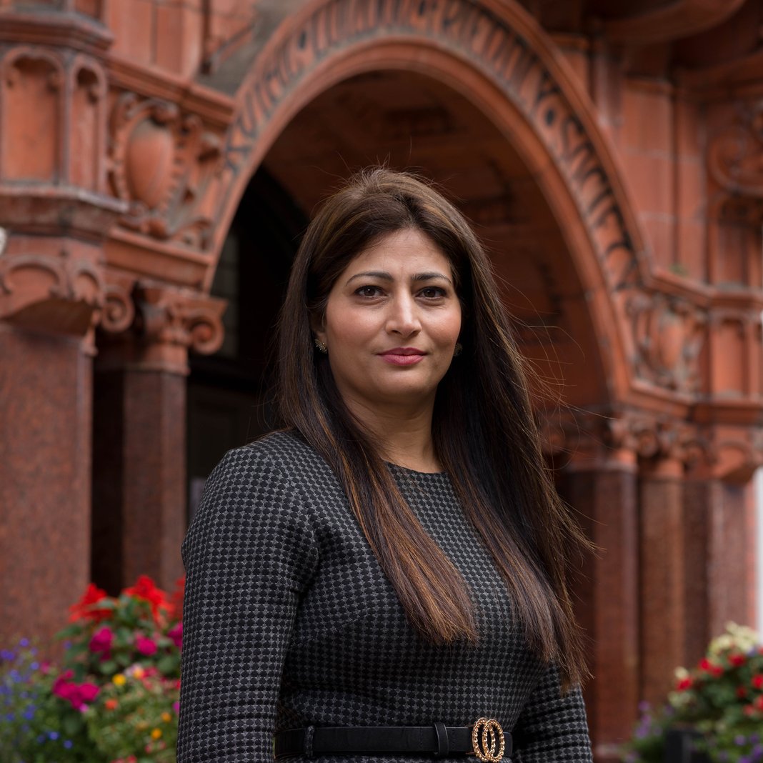 Councillor Nazia Rehman standing in front of a historic red stone building with arched entryway.