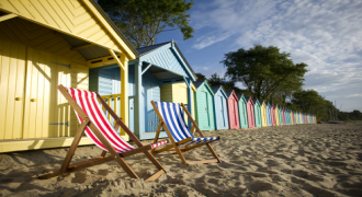 Picture of a beach with a row of beach huts and two deck chairs