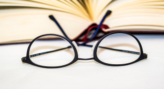 Picture of a pair of glasses next to a reading book