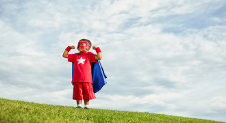 A picture of a boy dressed as a superhero standing on a hill